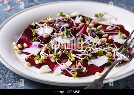 Vegetarische Rote-Bete-Carpaccio Salat mit Olivenöl, Ziegenkäse, Pinienkernen und Rosenkohl in weißer Teller über blaue Textur Hintergrund. Bis zu schließen. gesund Stockfoto