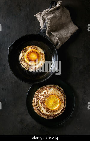 Hausgemachte Pfannkuchen mit gebratenen orange, im Cast-iron Pan und schwarze Platte auf dunklem Hintergrund. top View mit Platz Stockfoto