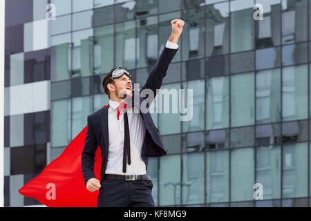 Ein Superheld Geschäftsmann hebt seine Hand gegen ein Geschäft Gebäude Hintergrund. das Konzept der Erfolg im Geschäft. Stockfoto