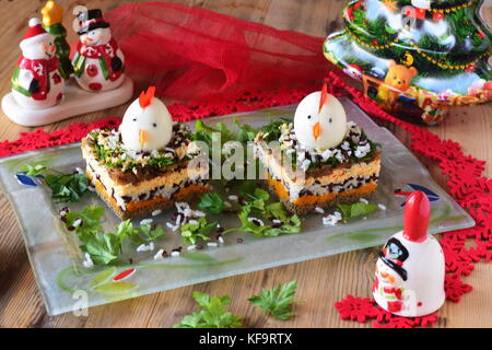 Salat in Schichten mit Hühnerleber, Zwiebeln, Karotten, schwarzer und weißer Reis, Petersilie und Dill mit Huhn den Kopf von gekochten Eiern dekoriert Stockfoto