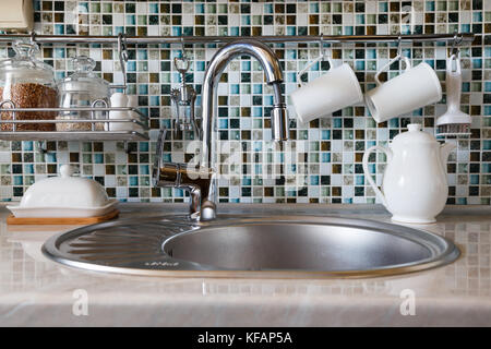 Modernes Geschirr und Utensilien wie Becher, Tassen, Tee- und Gläser mit Getreide um tippen und ein Waschbecken. Stockfoto