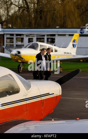 Ein rot lackiert Cabair Piper PA -28-161 Cadet und ein Gelb lackiert Piper PA -28-161 Cherokee Krieger 3 mit zwei Piloten gehen auf das Vorfeld und die Fliegenden Stockfoto