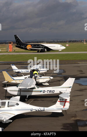 Ein Titan Airways Boeing 737-300 das Rollen mit einer Diamond DA40 Diamond Star TDI, Cessna 172 M, Piper PA-28 Cherokee und Cessna 152 Licht - Flugzeuge geparkt o Stockfoto