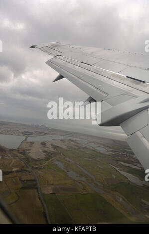 An den Landeklappen und Flügel der Titan Airways Boeing 737-300 Fliegen in der Nähe der Küste, Felder und Dungeness Kernkraftwerk auf einem grauen - Bewölkt Stockfoto