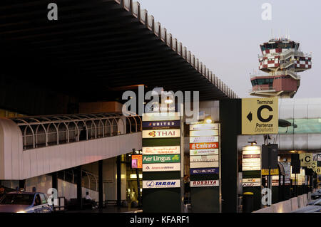 Anzeichen für Airlines, Klemmeb und TerminalC in englischer und italienischer Sprache mit dem Terminal und der Luftverkehrskontrolle - Tower hinter Stockfoto