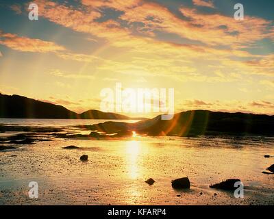 Spaziergang im Sonnenuntergang am Strand. Spiegelung von sunsetting Horizont im Meer Wasser zwischen Felsen. glatte Meer mit Feuern Himmel. die Sonne goldenen Licht ein Stockfoto