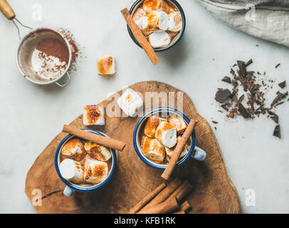 Heiße Schokolade in Emaille Becher mit Zimt und gerösteten Marshmallows über grauem Marmor Hintergrund, Ansicht von oben Stockfoto