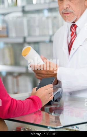 Frau, die NFC-Zahlung während Chemiker holding Shampoo Flasche Stockfoto