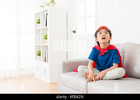 Schöne junge Kind Kinder Mädchen spielen Sie als Superheld und sitzen auf Wohnzimmer Sofa Couch entspannt zu Hause träumen. Stockfoto