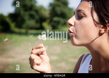 Junge Frau bläst Löwenzahn im Feld. Stockfoto