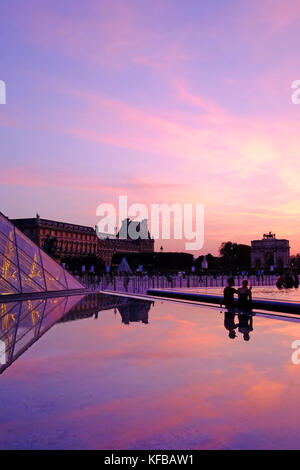 Ein junges Paar sitzen in der Nähe der Pyramide des Louvre bei Sonnenuntergang in Paris, Frankreich Stockfoto