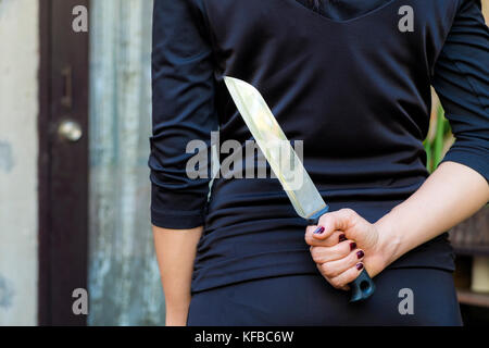 Frau in Schwarz mit einem Messer versteckt hinter Stockfoto