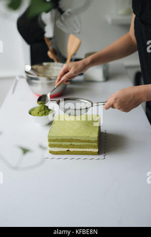 Grüner Tee Pulver über leckeren Käsekuchen gießen Stockfoto