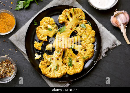 Gebratener Blumenkohl Steak mit Kräuter und Gewürze auf schwarzen Stein Hintergrund. top View Stockfoto