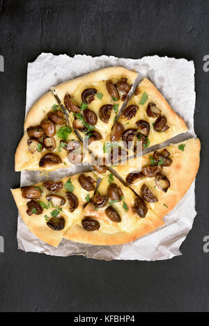 Geschnitten Pizza mit Pilzen und Käse auf dem Papier auf schwarzem Hintergrund, Ansicht von oben Stockfoto