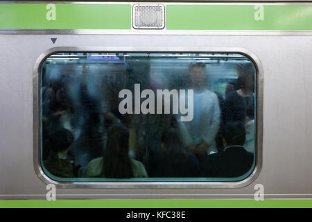 Pendler durch ein regnerisches und verputztes Fenster eines Yamanote Line-Zuges vom Shinjuku-Bahnhof, Tokio, Japan. Stockfoto