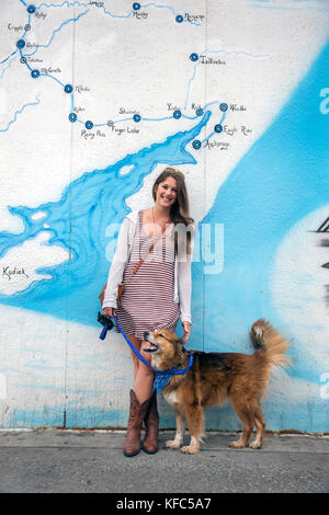 Usa, Alaska, Anchorage, lokale Lauren stellt mit ihrem Hund vor dem Iditarod Wandbild in der Innenstadt von Anchorage Stockfoto
