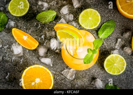 Vitamin Sommer erfrischende Getränke. Citrus punch mit Orangen und Kalk, mit Minze Zweige, gekühlt mit Eis. Auf schwarz Tisch aus Stein, mit Zutaten, kopieren Stockfoto