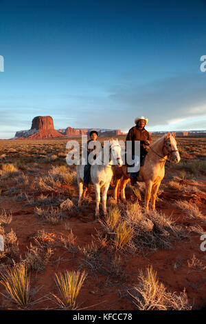 Usa; Arizona; Monument Valley, Navajo Tribal Park, ein Navajo Mann und sein Sohn reiten mit Mitchell Butte und Mitchell Mesa in der Ferne Stockfoto