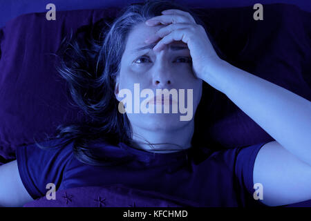 Frau mittleren Alters wach in ihrem Bett lag, nachts wegen der Schlaflosigkeit, Stress, Ängste, Alpträume oder Erkrankungen wie Fibromyalgie Stockfoto