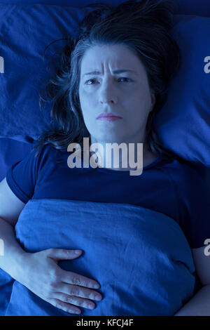 Frau mittleren Alters wach in ihrem Bett lag, nachts wegen der Schlaflosigkeit, Stress, Ängste, Alpträume oder Restless Leg Syndrom Stockfoto