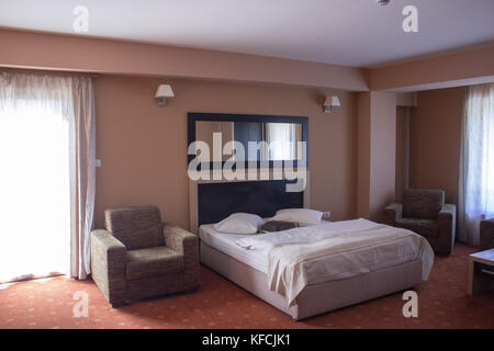 Zimmer im Hotel mit braunen Sessel und ein Doppelbett und einen roten Teppich und einer Wand an der Wand Stockfoto