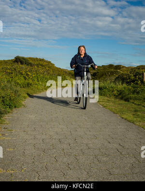 Dünen-Oase, Langeoog. Deutschland. Deutschland. Eine unbenannte Straße in die Sanddünen auf der Ostseite der Insel von der Dünen-Oase Café führt. Urlaub touristische zurück Radfahren von den Dünen in Richtung der Stadt Langeoog. Touristen kommen nach Langeoog für die Landschaft, frische Luft für eine gute Gesundheit. Stockfoto