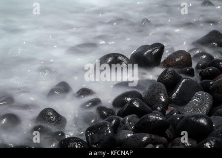 Pebble Beach auf der indonesischen Insel Bali. lange Belichtung Nahaufnahme der Flut und ihre Wirkung auf einer großen schwarzen Kieselsteinen mit misty Wasser Stockfoto