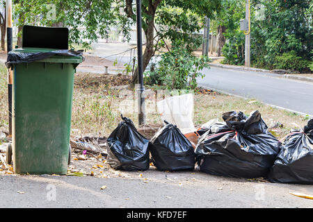 Alte große grüne Rad bin und Haufen von vollen Müllsäcke Stockfoto