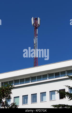 Große Handy rote und weiße Antenne Tower mit weißem Bürogebäude mit Bäumen vor es an einem warmen sonnigen Tag gelegen Stockfoto