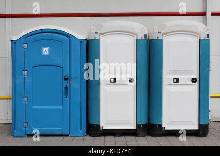 Drei tragbare Blau und Weiß ökologische Toiletten in einer Reihe von Männern, Frauen und Behinderte vor grauen Gebäude und auf Beton fliesen Stockfoto