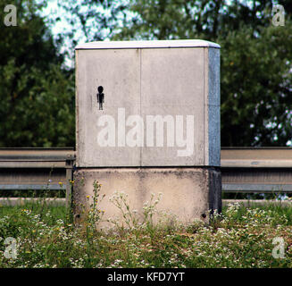 Kleine schwarze alien Suche graffiti auf Grau elektrische Feld in der Nähe von Autobahn und auf grünem Gras mit Blumen, lackiert Stockfoto