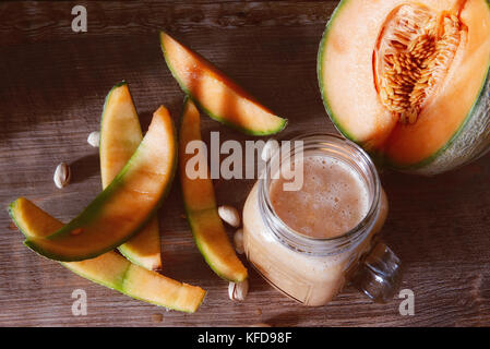 Leckere smoothies von Melone - Melone in einem Glas, ganze und aufgeschnittene Reif organische Melone - Melone auf hölzernen Hintergrund, rustikale gemütliche Atmosphäre. Stockfoto