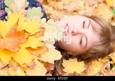 Eine nette junge Mädchen liegt auf Herbst Laub mit geschlossenen Augen, ein Bouquet von gelben Blätter im Herbst in den Händen Stockfoto