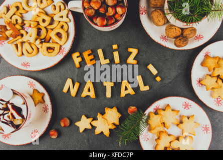 FELIZ NATAL COOKIES. Wörter Frohe Weihnachten en Portugiesisch mit gebackenen Plätzchen, Weihnachtsschmuck und Muttern auf schwarzem Schiefer Hintergrund. Christmas Card f Stockfoto