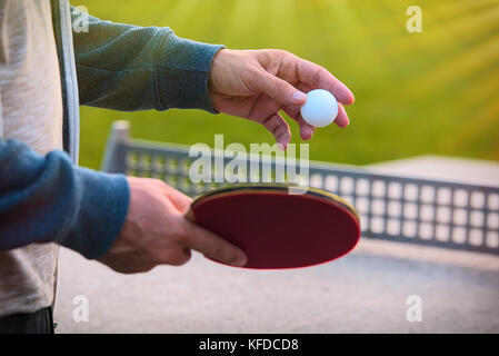 Der tennisspieler Hände mit Tennisschläger auf Natur Hintergrund im sonnigen Tag schließen. closeup Schoß eines Mannes im Tischtennis im Freien Tennis Registerkarte dienen. Stockfoto