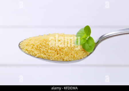 Löffel von rohen Couscous auf weißem Holz- Hintergrund Stockfoto