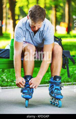 Junger hübscher Kerl Schnürsenkel binden auf seinem Inline Skates. Stockfoto