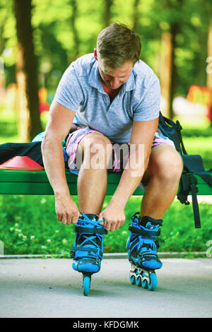 Junger hübscher Kerl Schnürsenkel binden auf seinem Inline Skates. Stockfoto