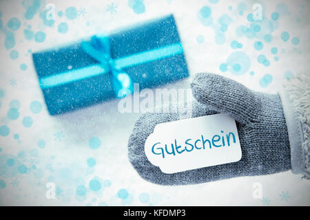 Handschuh mit Label mit deutschem Text Gutschein Gutschein bedeutet. türkis Geschenk oder auf Schnee im Hintergrund vorhanden. saisonale Grußkarten mit Schneeflocken und Stockfoto