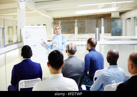 Reifer, selbstbewusster Lehrer, der während der Präsentation vor dem Publikum auf das Whiteboard zeigt Stockfoto