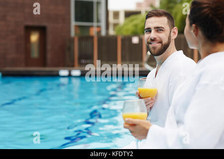 Glücklicher Mann, der während der Flitterwochen-Tour am Pool mit seiner Frau spricht Stockfoto