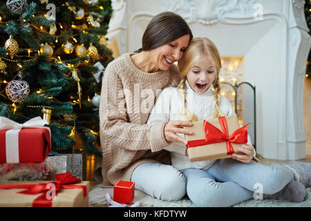 Überrascht Mädchen schauen in Geschenkverpackung mit Weihnachtsgeschenk von ihrer Großmutter Stockfoto