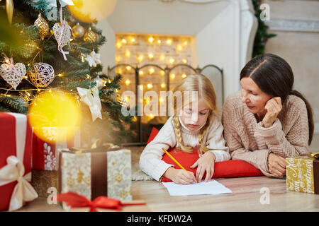 Süße kleine Mädchen schreiben Brief auf xmas Nacht mit ihrer Großmutter in der Nähe zu Santa Stockfoto