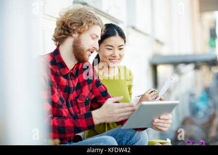 Junge freundliche Studenten, die Online-Daten für ihr Bildungsprojekt durchsuchen Stockfoto