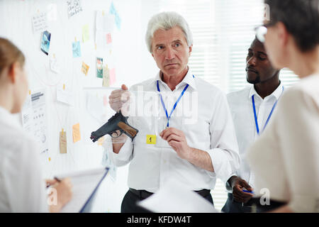 Reifen forensischen Prüfer mit Gewehr von Tatort zu seinen Kollegen beim Stehen an der Untersuchungskommission und die Teilnehmenden in der Diskussion Stockfoto