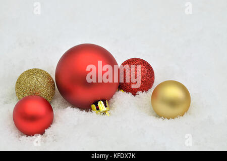 Nahaufnahme von roten und goldenen Weihnachtsbaum Kugel Ornamente auf Schnee Hintergrund Stockfoto