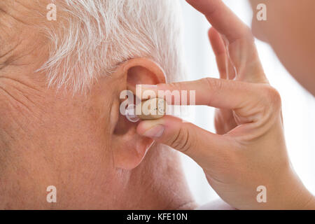 Nahaufnahme der Arzt das Hörgerät im Ohr des älteren Patienten Stockfoto