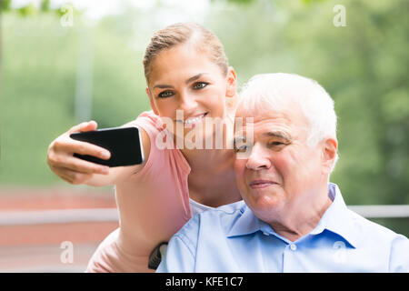 Nahaufnahme einer lächelnden jungen Frau mit ihrem Vater unter Selfie auf Handy Stockfoto