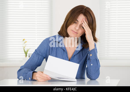 Traurige junge Frau liest Dokument in Office Stockfoto